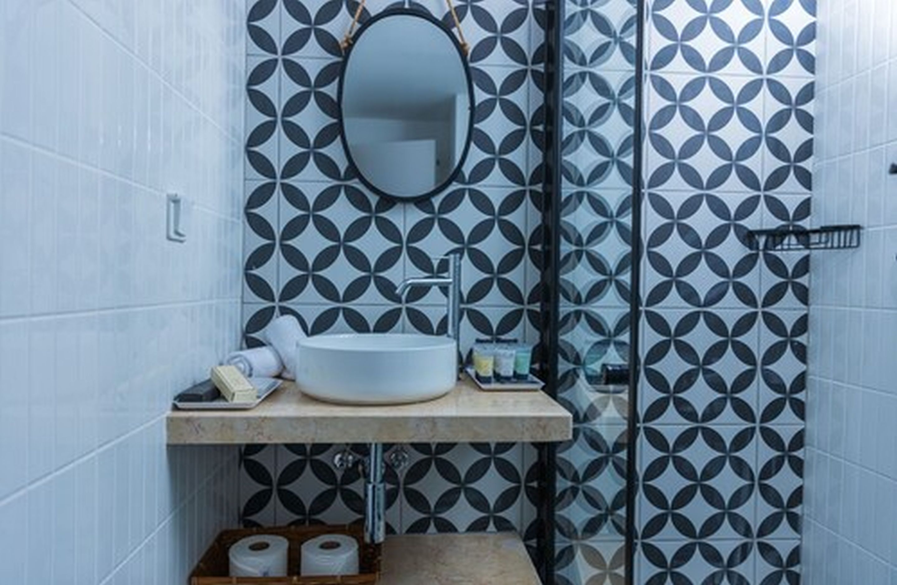 Casa de banho com uma pia branca, um espelho e azulejos estampados.
