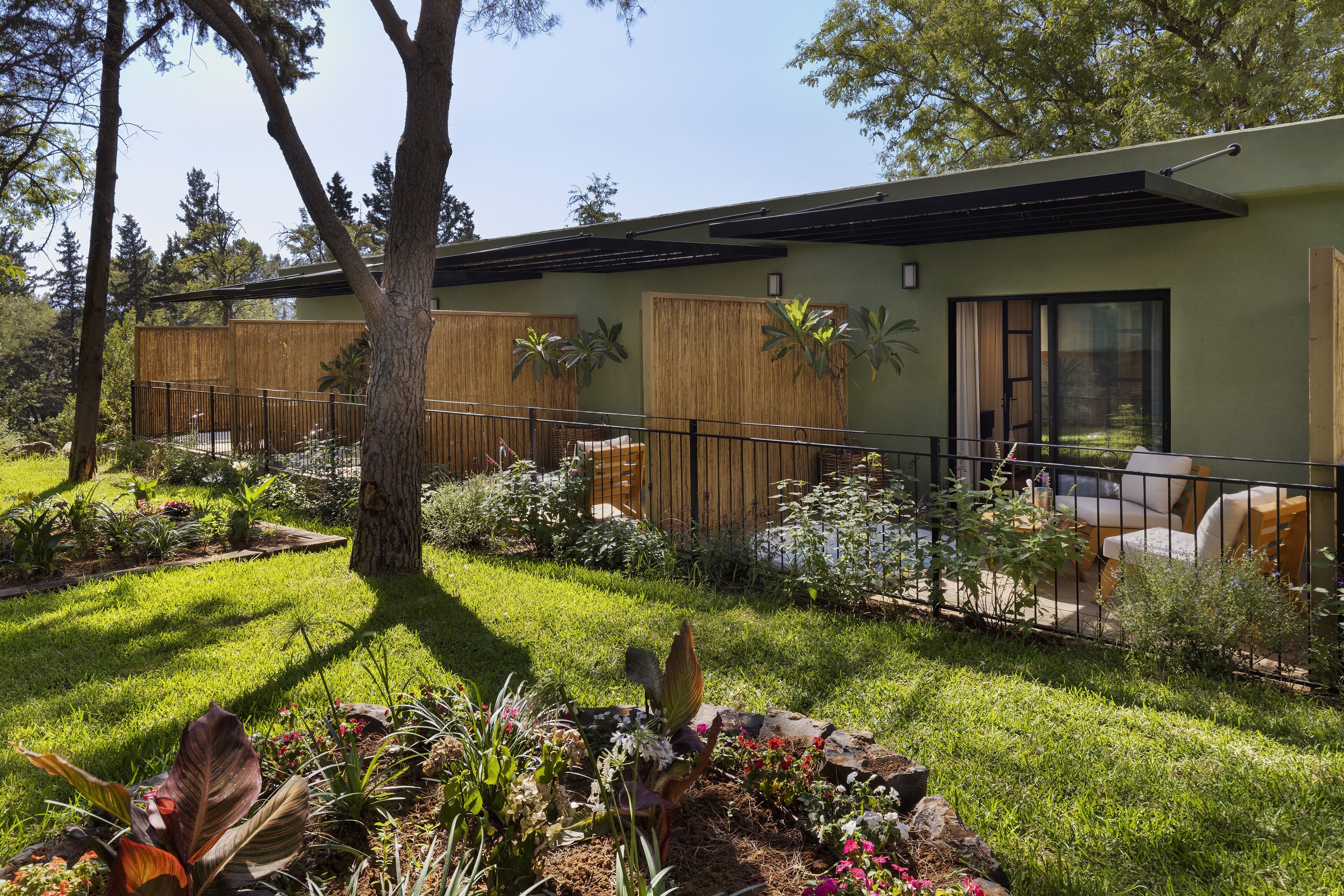 Una casa moderna con un porche cubierto, un jardín vallado y diversas plantas.