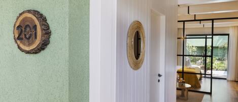 Een gang met een houten nummerbord, een geweven spiegel en een kamer met een bed en een tafel.