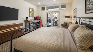 A bedroom with a bed, bedside table, lamp, and a desk with a computer and other items. - Downtown Hideaway in the Heart of Moab #2 (Moab)