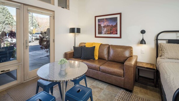 A cozy room with a brown leather sofa, a small round table with a plant, and a framed picture on the wall. - Downtown Hideaway in the Heart of Moab #2 (Moab)