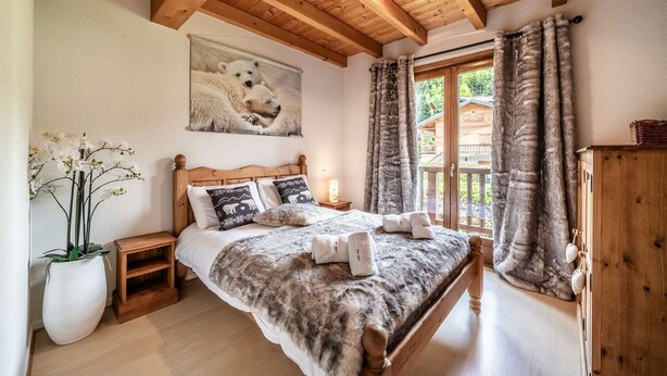 Ein Schlafzimmer mit einem hölzernen Bett, einem Nachttisch, einem großen Fenster mit Vorhängen, einem Gemälde von Eisbären und einer Topfpflanze.
