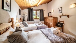Ein Schlafzimmer mit zwei Betten, Holz-Kopfteilen, einem Fenster mit Vorhängen, einem Holzschrank und Wandleuchten.