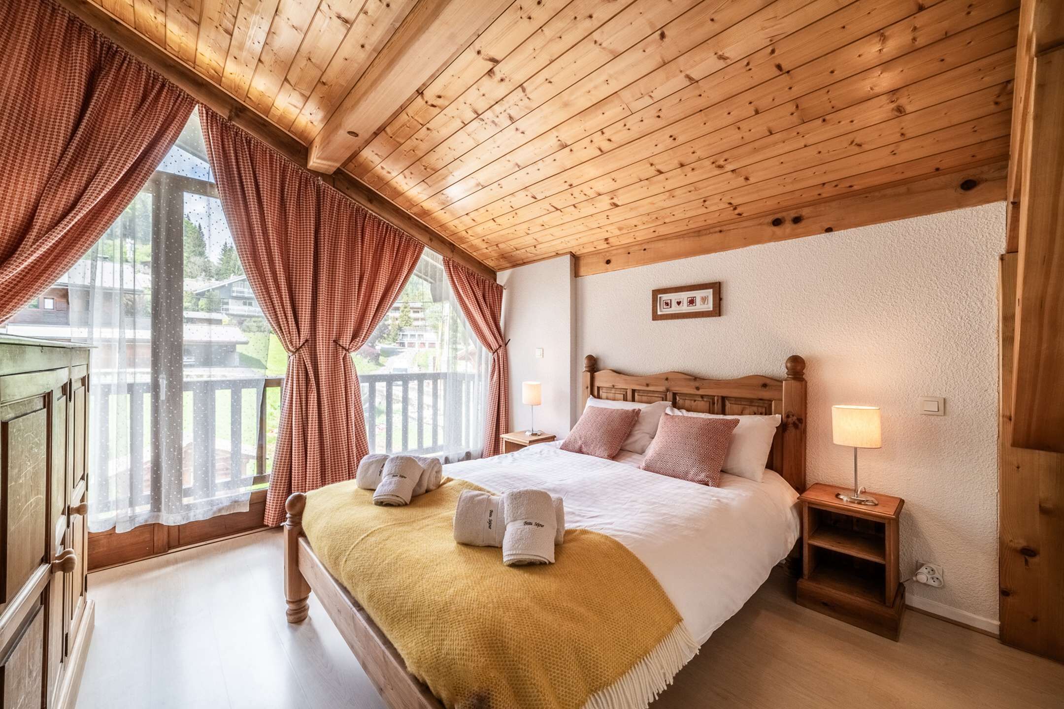 Ein Schlafzimmer mit Holzwänden, einem großen Bett, einem Nachttisch und einem Fenster mit Vorhängen.