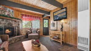Un salon chaleureux avec une cheminée en pierre, des murs en bois, un téléviseur et un coin salon confortable.