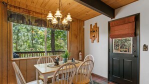 Un intérieur en bois comprenant une table et des chaises, un lustre, une fenêtre donnant sur des arbres et une porte avec un panneau en bois.