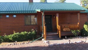 Une cabane en rondins avec un toit en métal vert, une véranda en bois et une enseigne sur laquelle on peut lire « Cozy Bear ».