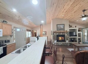 A spacious kitchen with a long island, wooden ceiling, and a stone fireplace. - Cozy Bear Cabin with Hot Tub (overgaard)