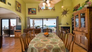 A dining area with a large table, chairs, a ceiling fan, and a view of the ocean through the glass doors. - Ocean view 6 bedroom 4 bath 3500 square foot  (Puerto Penasco)
