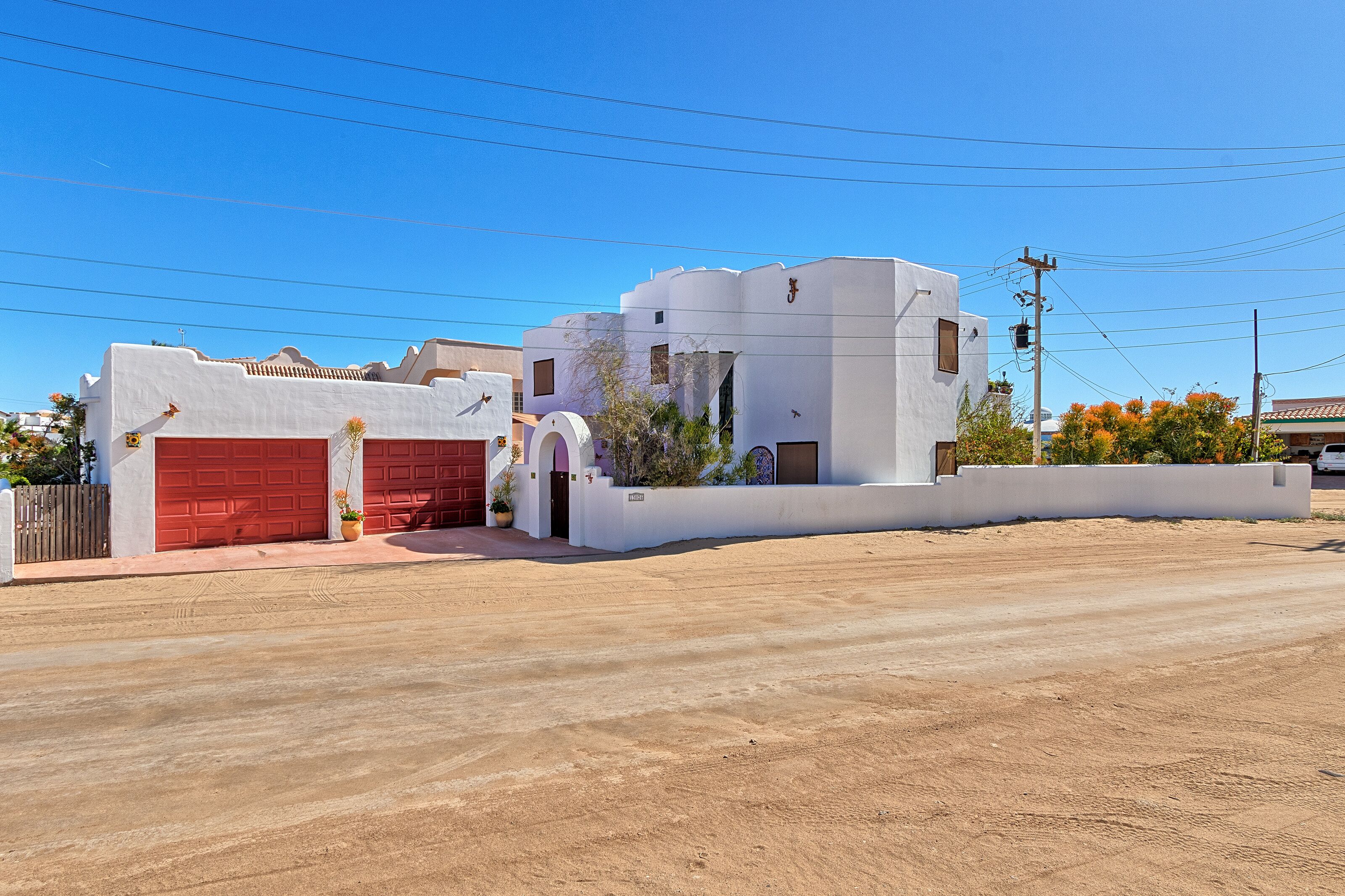 Un bâtiment moderne de couleur blanche, doté d’une porte de garage rouge, entouré d’une zone sablonneuse.