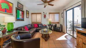 A living room with a sectional sofa, a glass coffee table, a ceiling fan, and a large window with a view of the city. - Ocean view 6 bedroom 4 bath 3500 square foot  (Puerto Penasco)