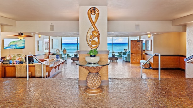 En lobby med receptionsdisk, en dekorativ infinity-skulptur, en potteplante og udsigt til havet.