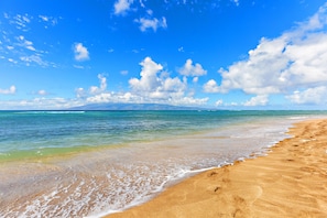 Enjoy the serene beach scene with gentle waves lapping at the shore and a majestic mountain range in the distance.