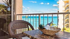 En fletstol og et bord med en flaske og glas på en balkon med udsigt over havet.