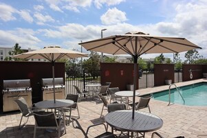 Zona junto a la piscina con mobiliario exterior, una parrilla y sombrillas.