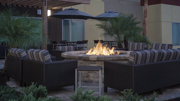An outdoor patio with wicker furniture, a stone fire pit, and umbrellas. - TownePlace Suites by Marriott Titusville Kennedy Space Center (Titusville)