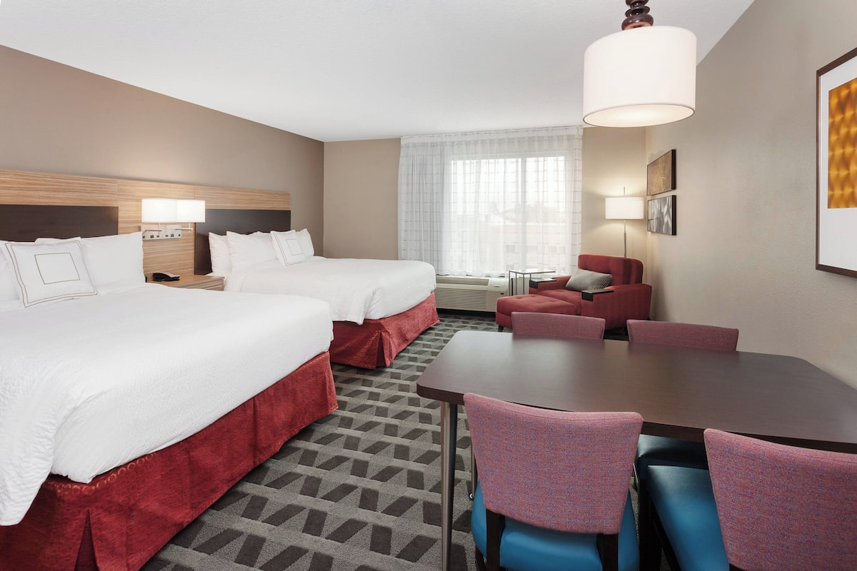 A hotel room with two beds, a dining table, and a sofa.