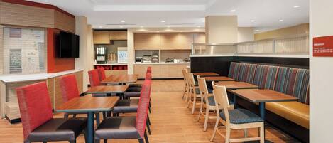 Un restaurante moderno con suelo de madera, sillas tapizadas en rojo y diversas opciones de asientos, incluyendo reservados y mesas.