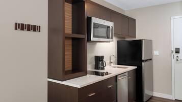 Una cocina moderna con armarios de madera oscura, un refrigerador de acero inoxidable, un microondas integrado y una cafetera.