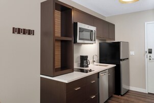 Una cocina moderna con armarios de madera oscura, un refrigerador de acero inoxidable, un microondas integrado y una cafetera.