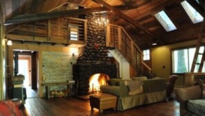 Un intérieur rustique avec une cheminée en pierre, des poutres en bois, un escalier et un coin salon confortable.