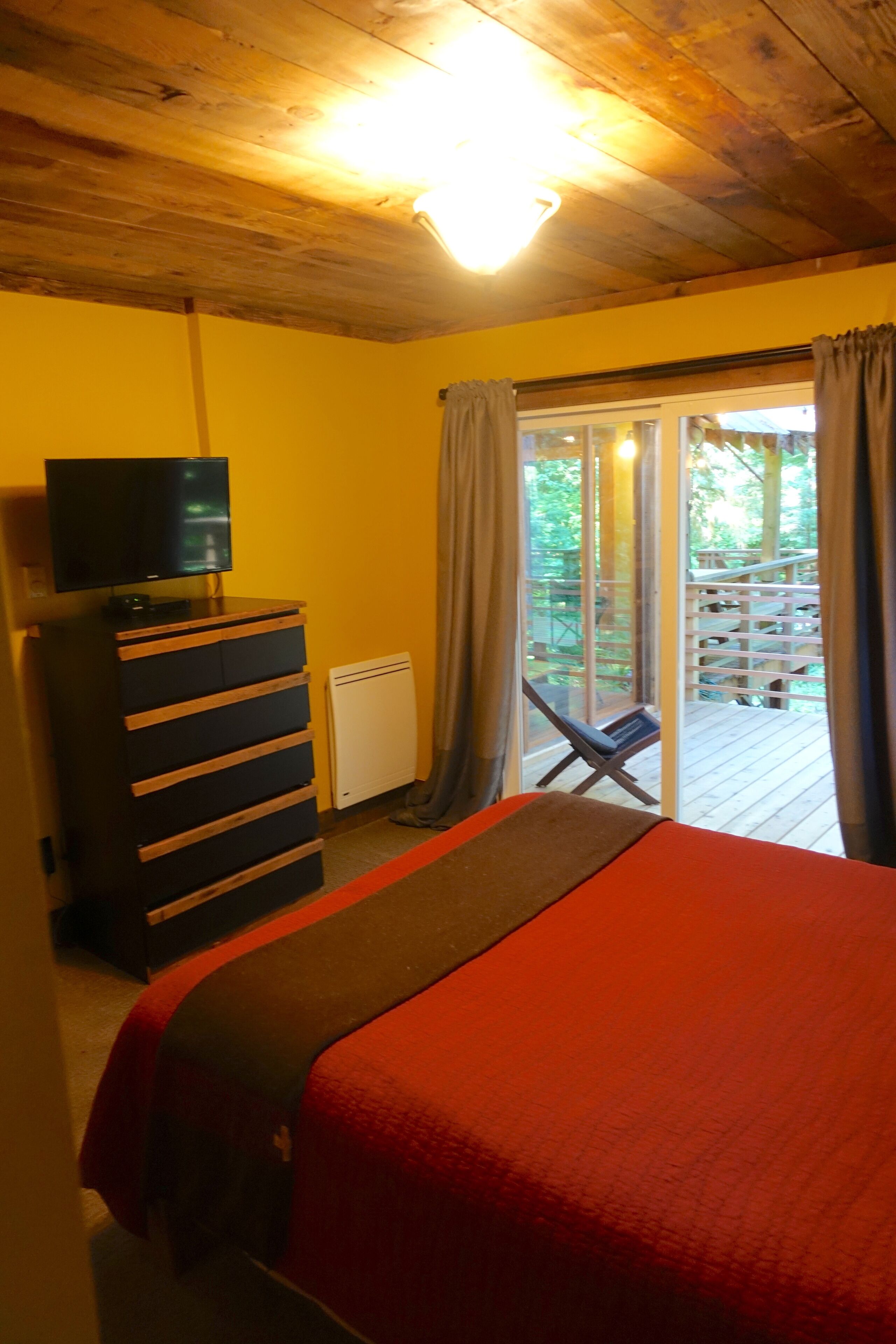 A room with a bed, a dresser, a television, and a sliding glass door leading to an outdoor deck.