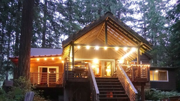 Une cabane en bois avec un escalier menant à une terrasse, entourée d’une forêt dense.