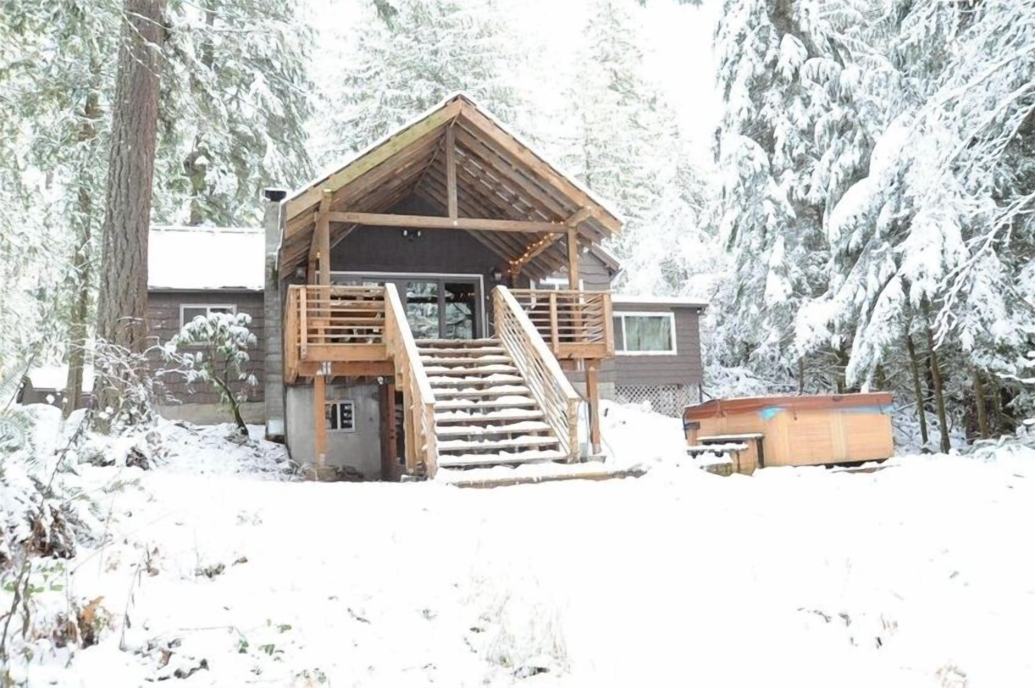 A wooden cabin with a staircase leading to a porch, surrounded by snow-covered trees.
