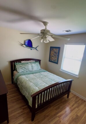 A bedroom with a wooden bed, a ceiling fan, a window with blinds, and a wall-mounted fish decoration.