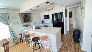 A kitchen with a central island, bar stools, a refrigerator, and a microwave.
