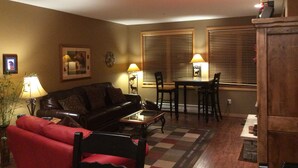 A living room with a sofa, a red chair, a coffee table, and a dining area with a table and chairs. There are two lamps on the table and a clock on the wall. - Roomy 2BR/2BA in Keystone (Keystone)