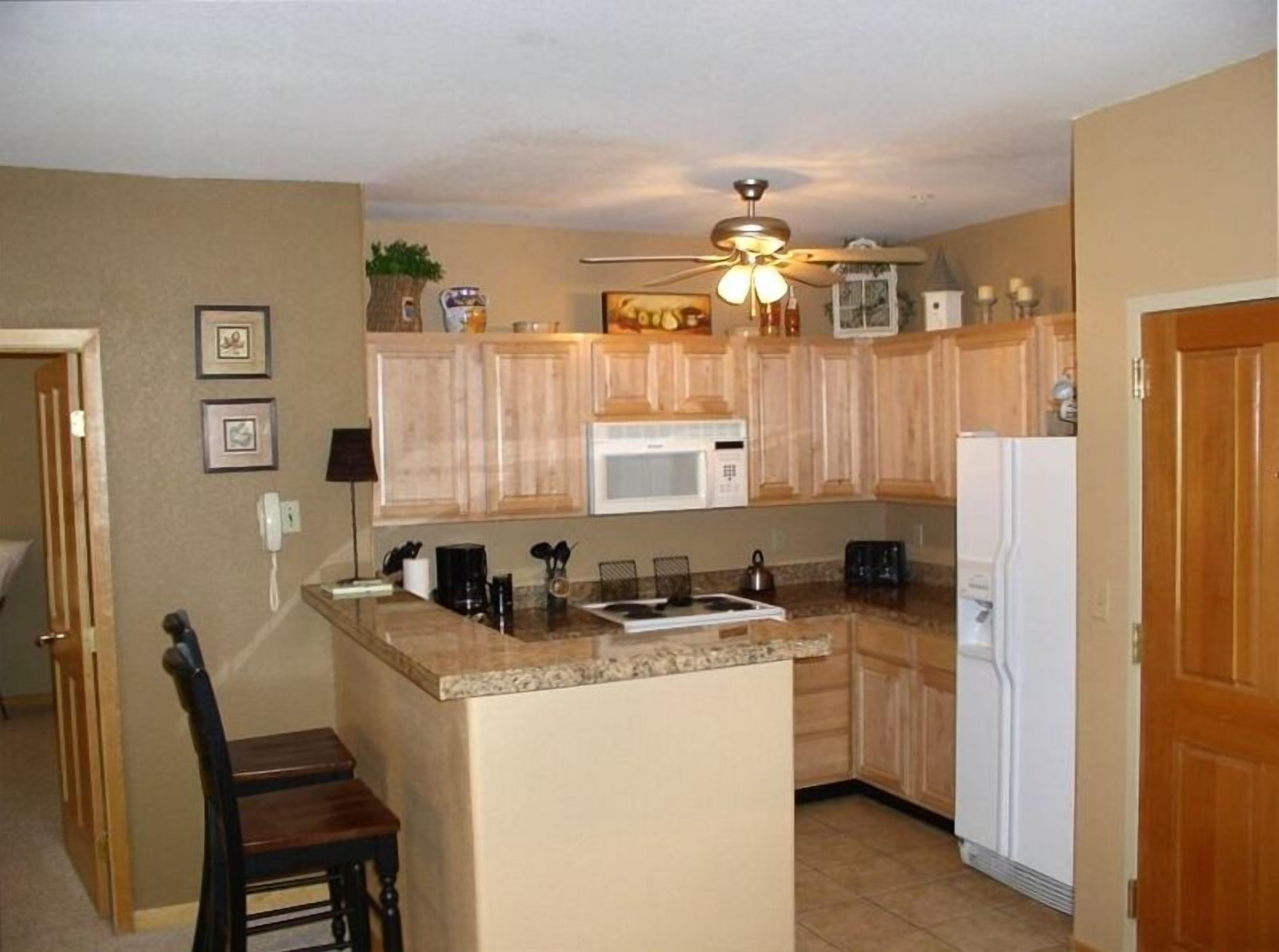 Una cocina compacta con armarios de madera, microondas, refrigerador y ventilador de techo.