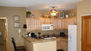 A compact kitchen with wooden cabinets, a microwave, a refrigerator, and a ceiling fan. - Roomy 2BR/2BA in Keystone (Keystone)