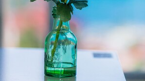 Una botella de vidrio transparente con una sola rosa roja sobre una superficie reflectante.