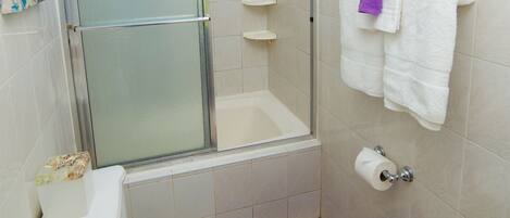A bathroom with a glass-enclosed shower, a toilet, a bathtub, and a purple bath mat.