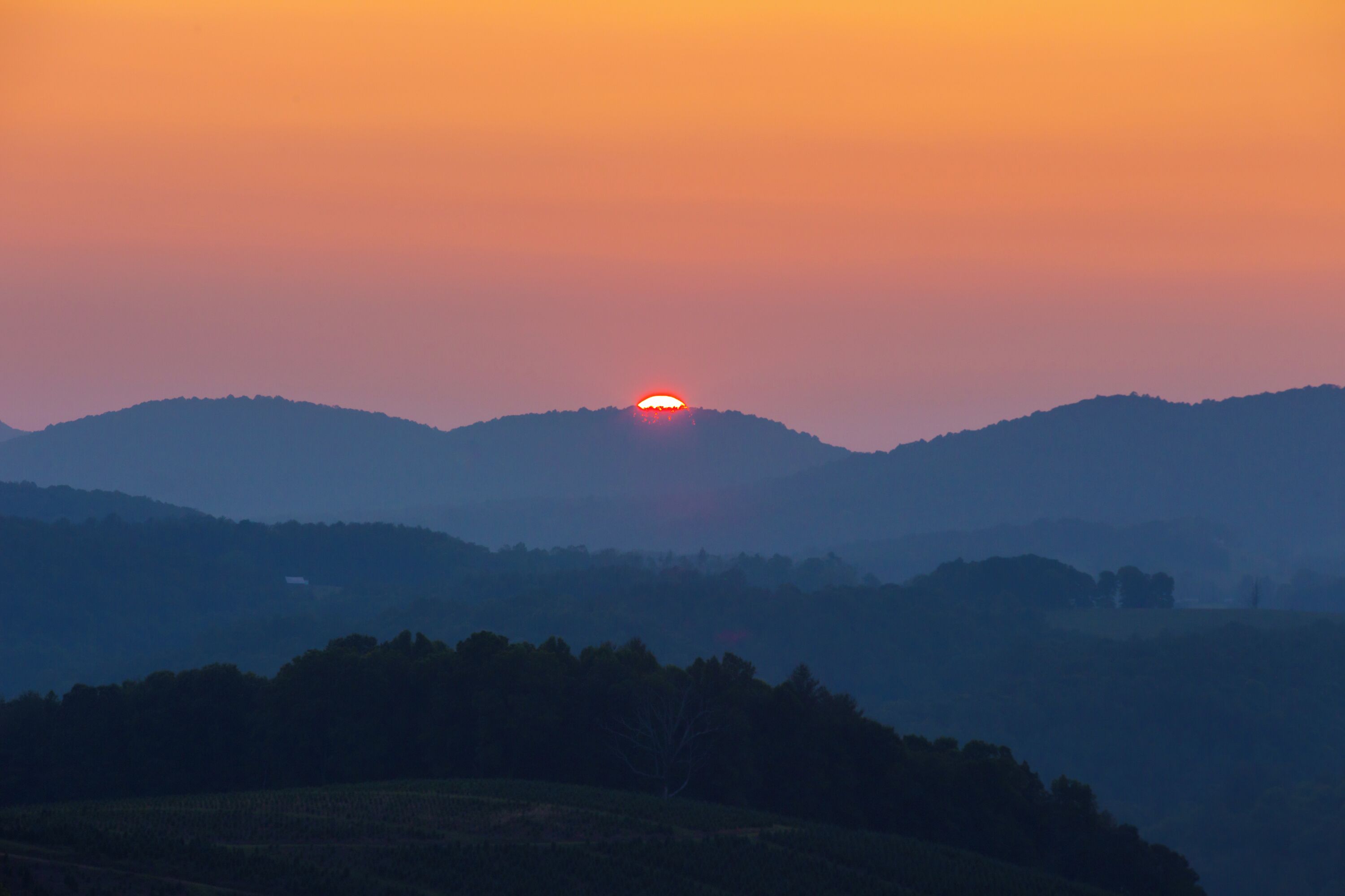 Un coucher de soleil sur une chaîne de collines, avec un ciel dégagé.