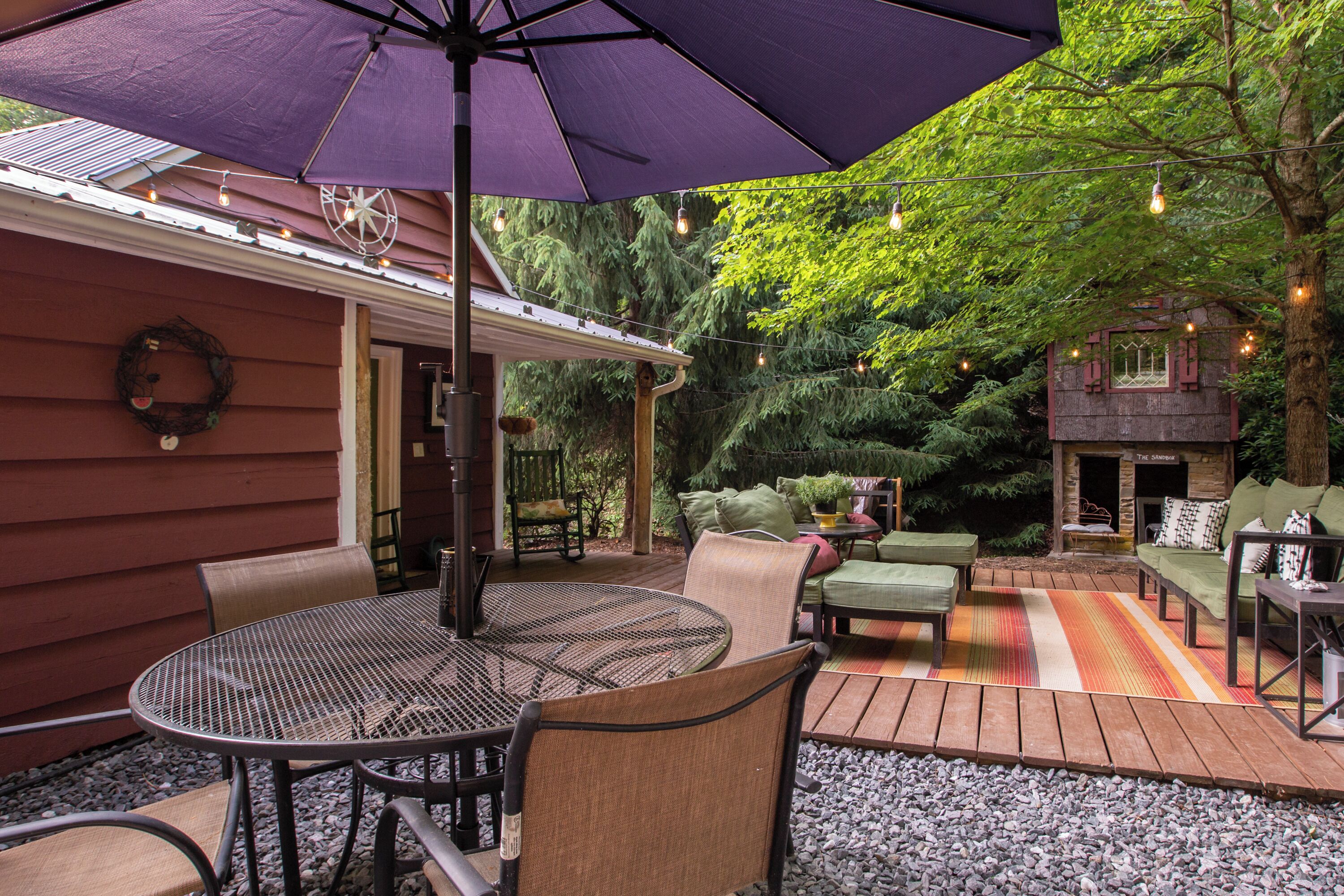 Un espace extérieur aménagé en terrasse, avec une table ronde et des chaises, un parasol violet et une plateforme en bois.