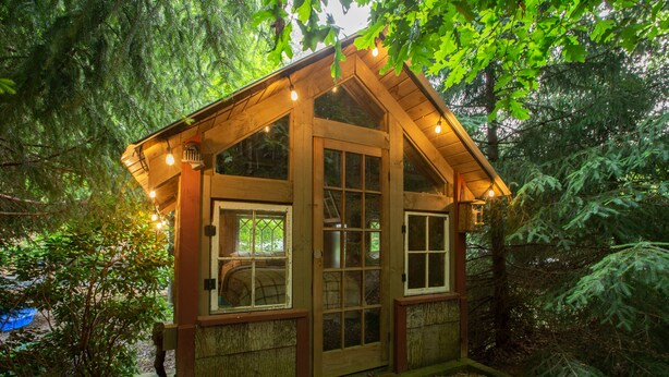 Eine Holzhütte mit vielen Fenstern und einem geneigten Dach, umgeben von dichtem Wald.