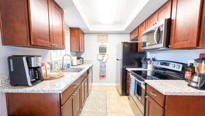 A compact kitchen with wooden cabinets, a built-in microwave, a coffee maker, and a stove. - Bright*Private*Stylish 2BR Flat W/ Fenced Yard Near Washington Square (Tigard)