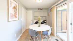 A dining area with a round table, chairs, a vase with flowers, and a laundry sign on the wall. - Bright*Private*Stylish 2BR Flat W/ Fenced Yard Near Washington Square (Tigard)