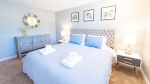 A neatly made bed with a blue and white striped bedspread, two pillows, and a folded towel. There is a gray dresser with a mirror above it, a bedside table with a lamp, and three framed pictures on the wall. - Bright*Private*Stylish 2BR Flat W/ Fenced Yard Near Washington Square (Tigard)