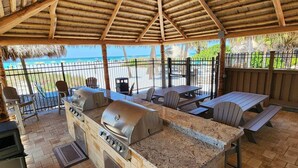 An outdoor barbecue area with a stone grill, seating, and a view of the beach. - On the Beach! Updated 2bd/2bth. Escape the cold, spend Christmas in Paradise! (Siesta Key)