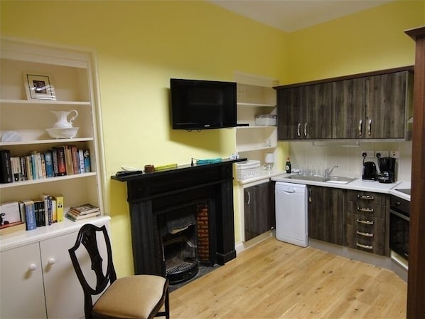 Cozy living space with a fireplace, TV, and dining area, featuring a well-equipped kitchen with a dishwasher and coffee maker.