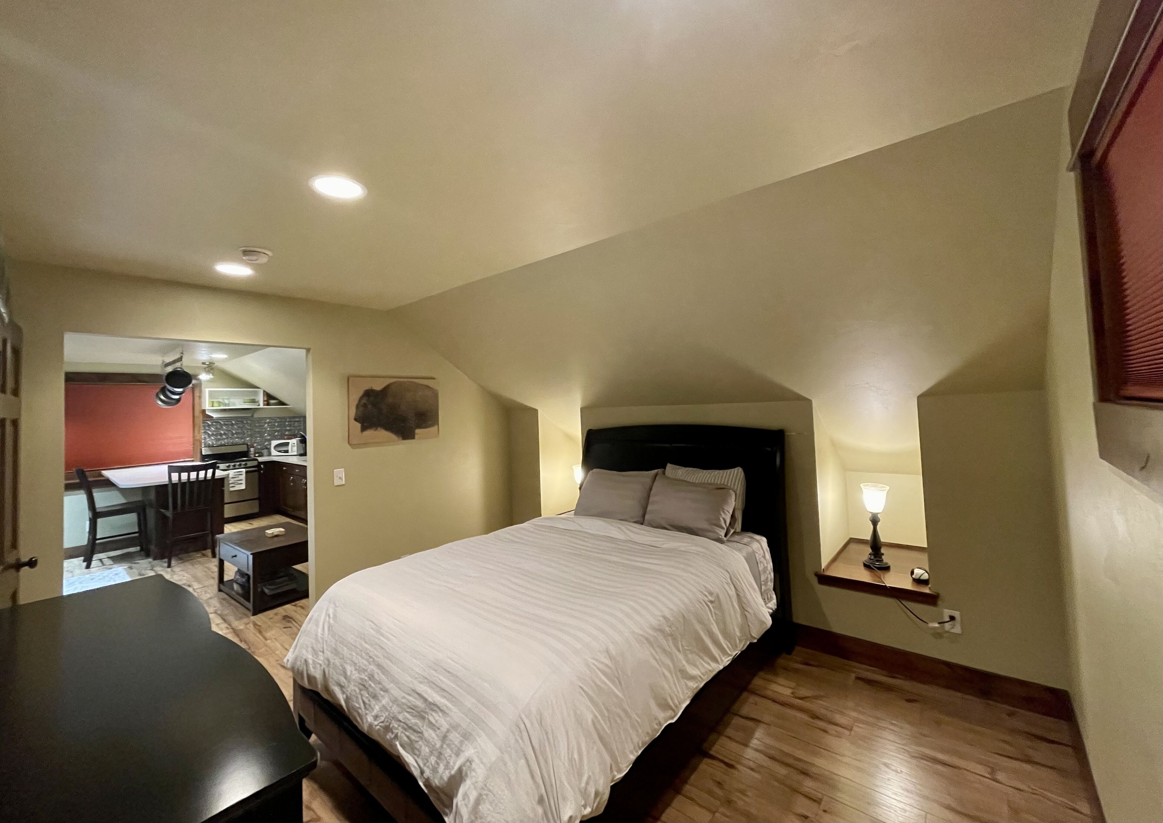 Un dormitorio con una cama, un escritorio y una kitchenette al fondo.