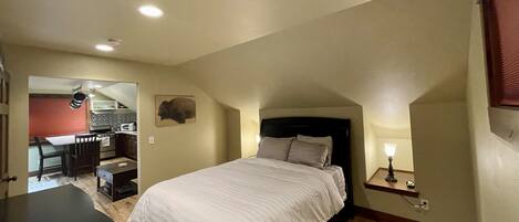 Un dormitorio con una cama, un escritorio y una kitchenette al fondo.