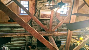 Ein rustikales Blockhaus-Interieur mit freiliegenden Holzbalken, Steinwänden und einer Holztreppe.