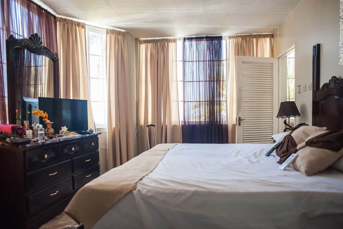 Quarto de hotel com cama, cômoda, televisão e cortinas.
