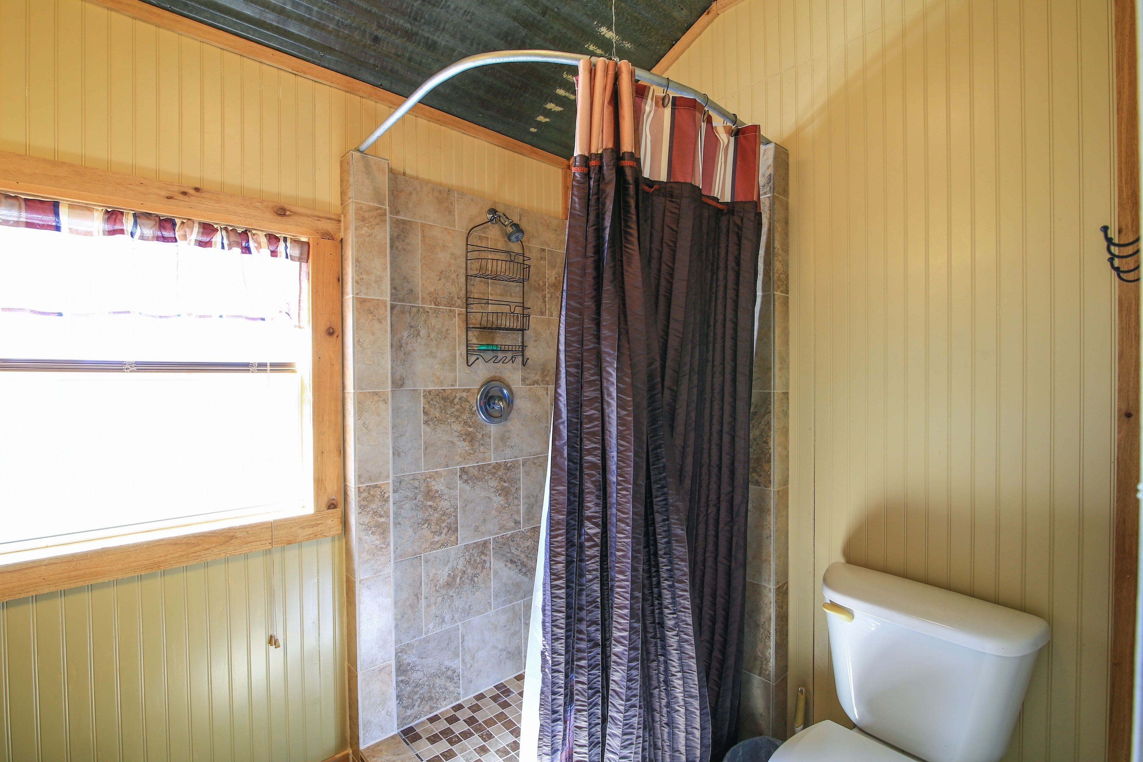 A bathroom with a shower, toilet, and a window with a curtain.