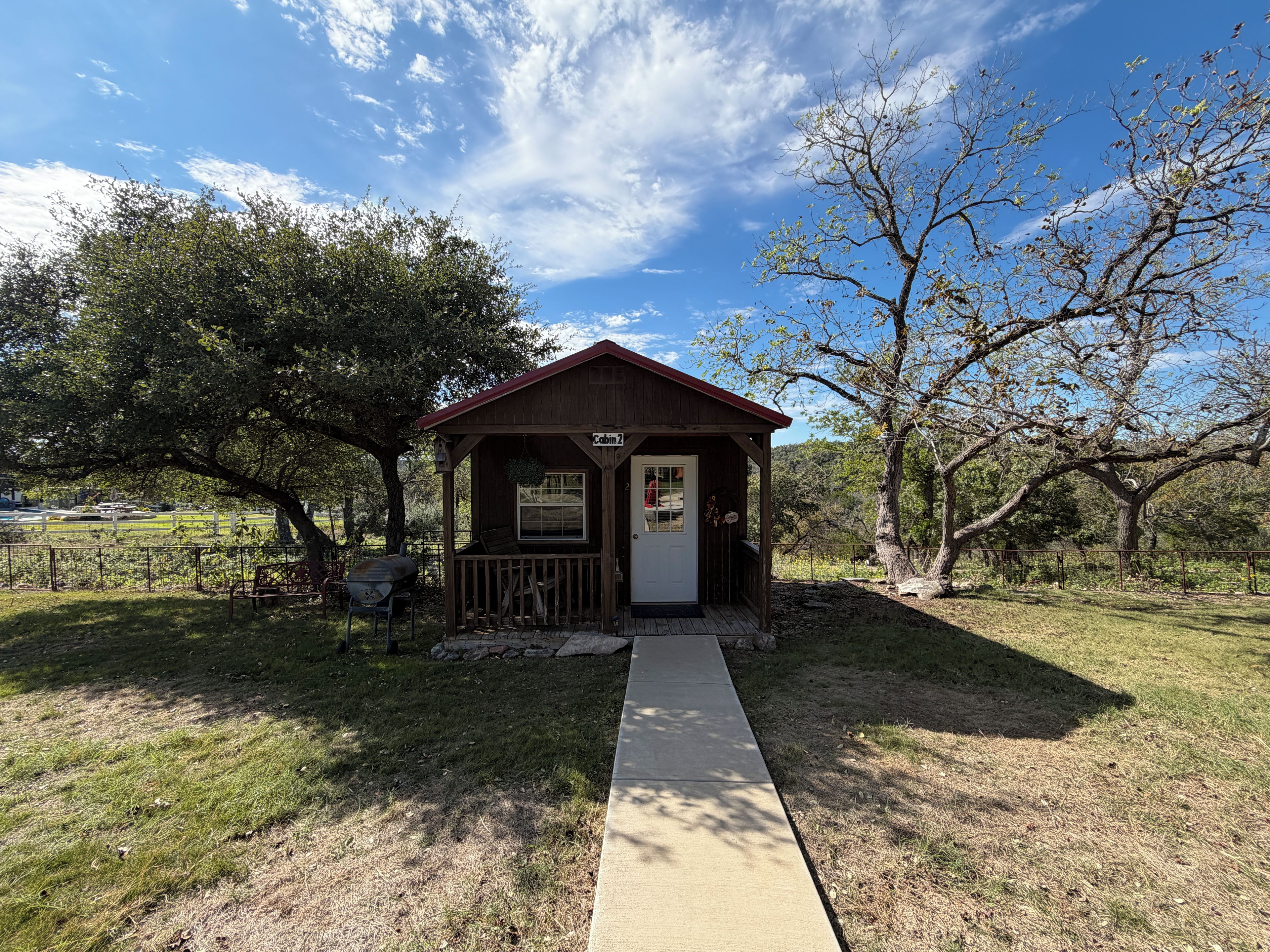 A small wooden cabin with a porch, labeled 'Cabin 2,' situated in a grassy area with trees.