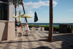 An outdoor patio with tables and chairs, a palm tree, and a view of the ocean. - Beachside Villa - Ocean 100 Ft. (Deerfield Beach)